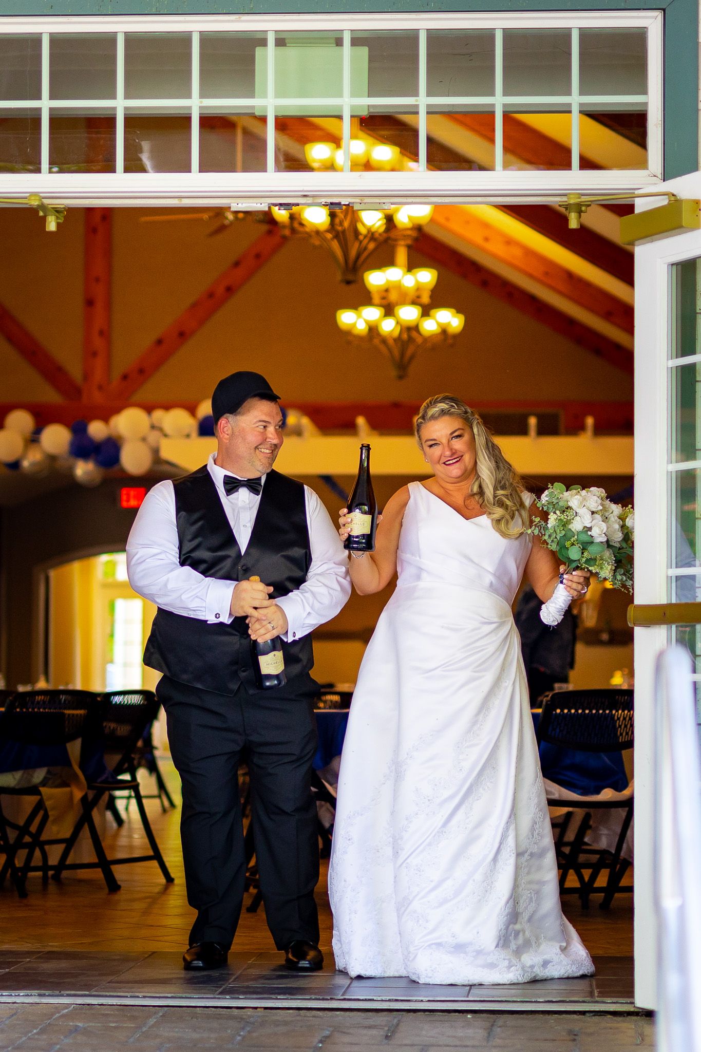 Newlyweds make their grand entrance into a warmly lit reception hall with chandeliers.
