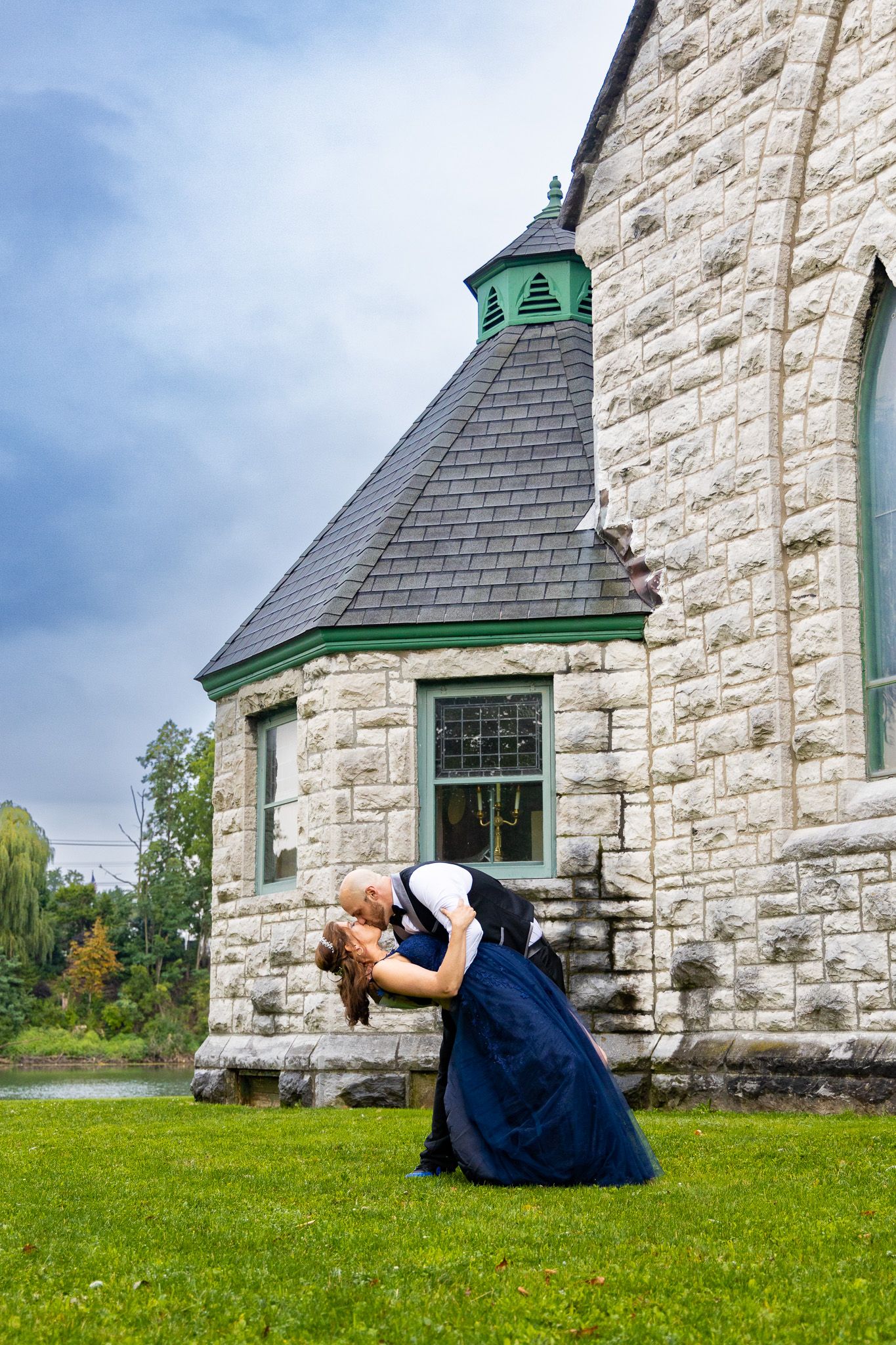 A romantic dip pose in front of a stone church with green trim.
