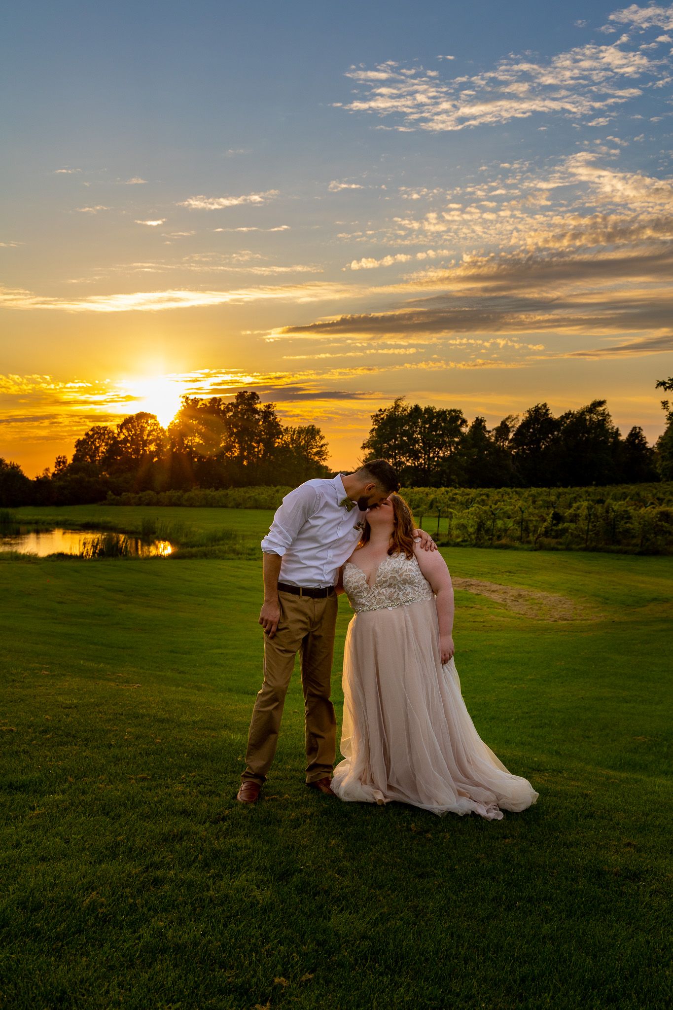 A couple shares a romantic moment at sunset on a golf course near a pond.