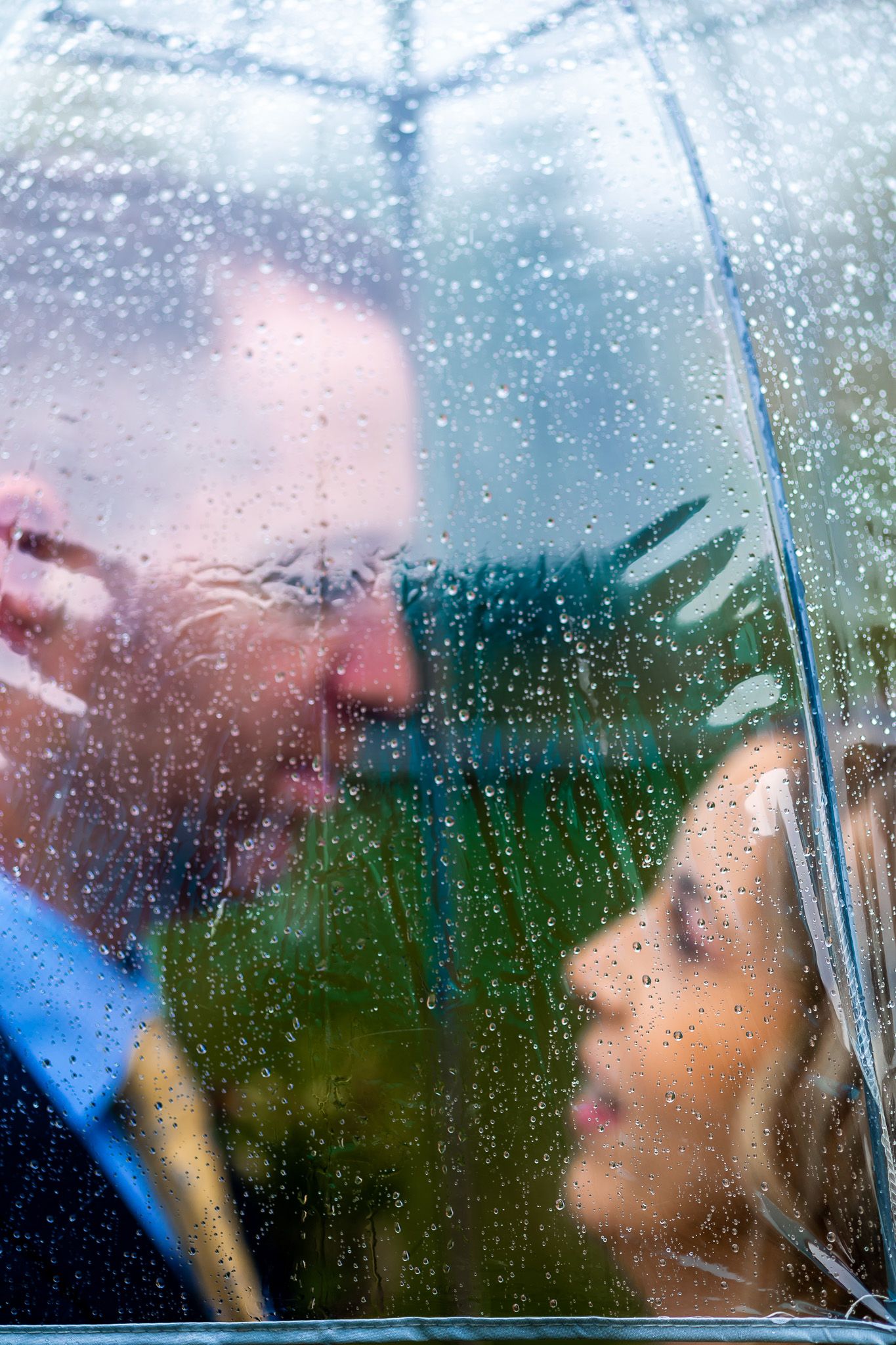 Romantic rainy day portrait through a rain-covered window with dreamy bokeh effect.