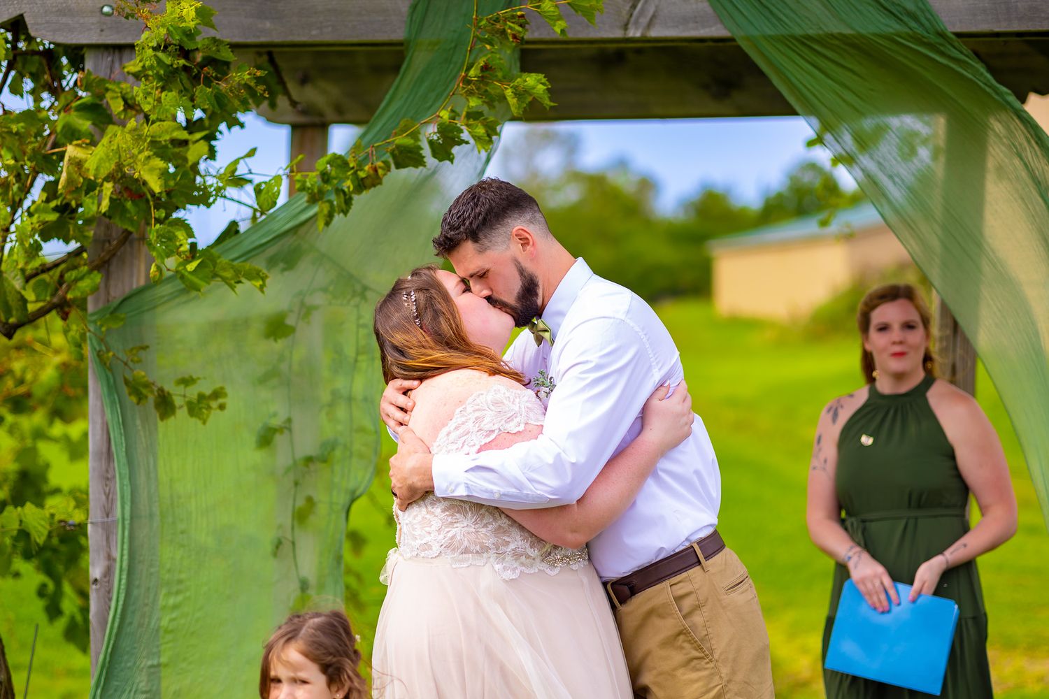 An intimate wedding ceremony moment under a wooden pergola in a garden setting.
