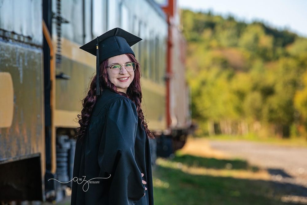 A graduation photo taken near a vintage train car with trees in the background.