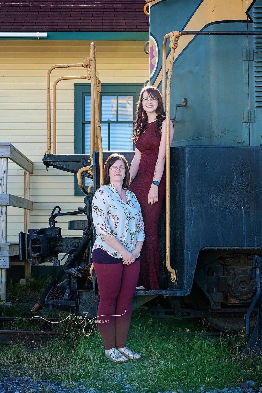 Two people posing next to a vintage train car on a sunny day.