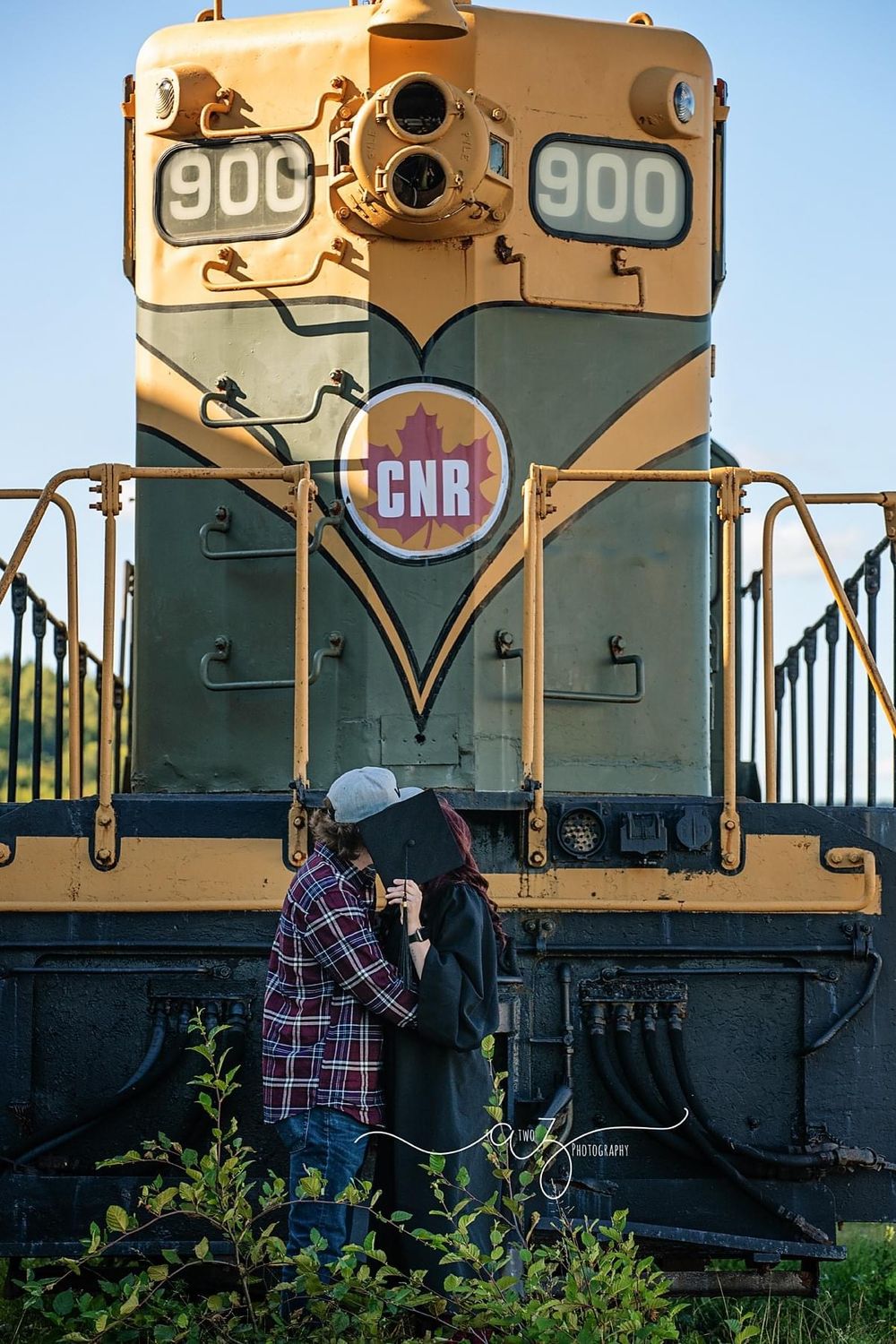 Two people standing in front of a CNR locomotive number 900 during golden hour.