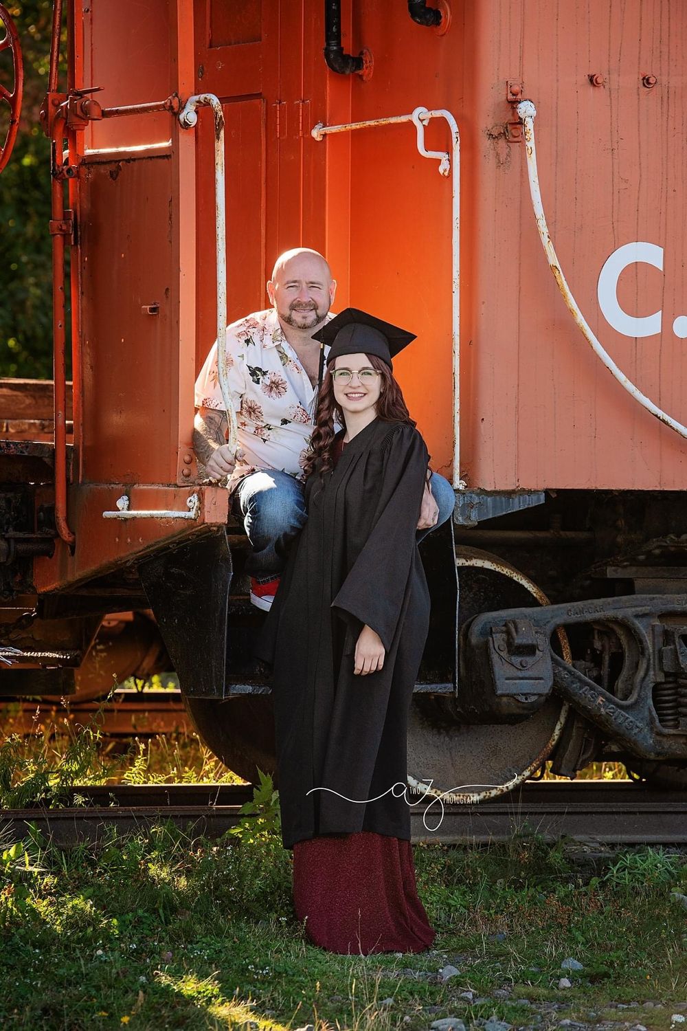 A graduation photo featuring two people posing on a red vintage train caboose.