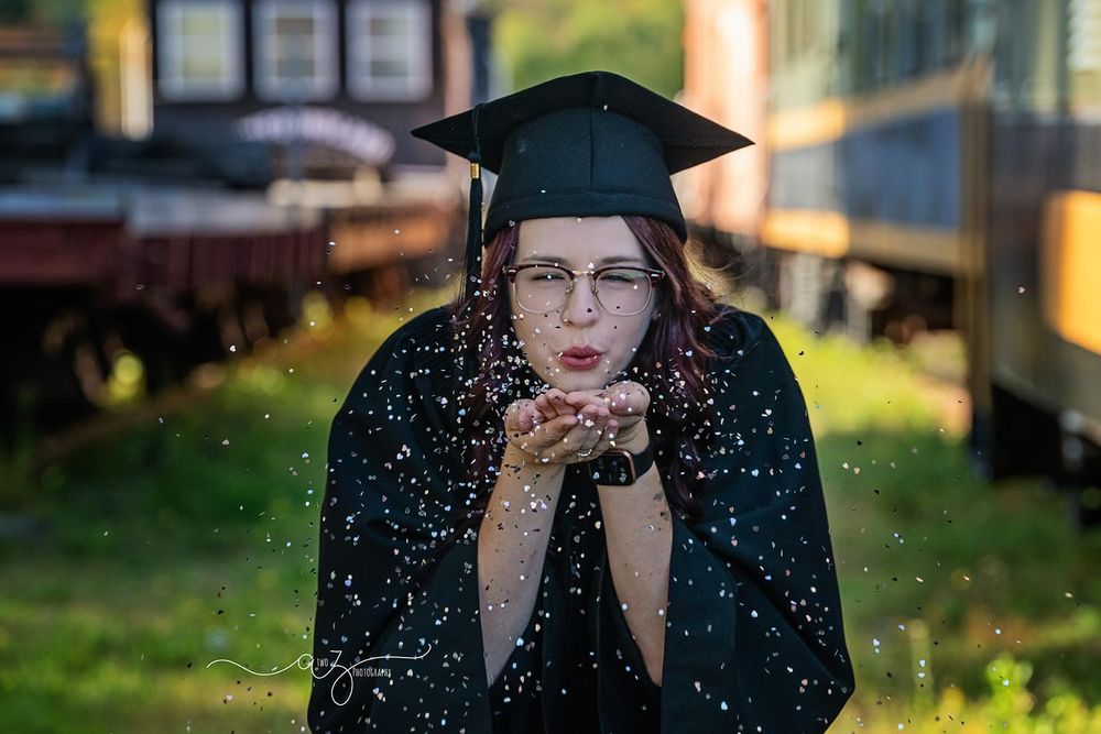 A graduation portrait with glitter being blown in front of vintage train cars.