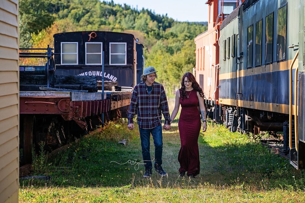 A couple walking between vintage train cars in an outdoor railway setting.