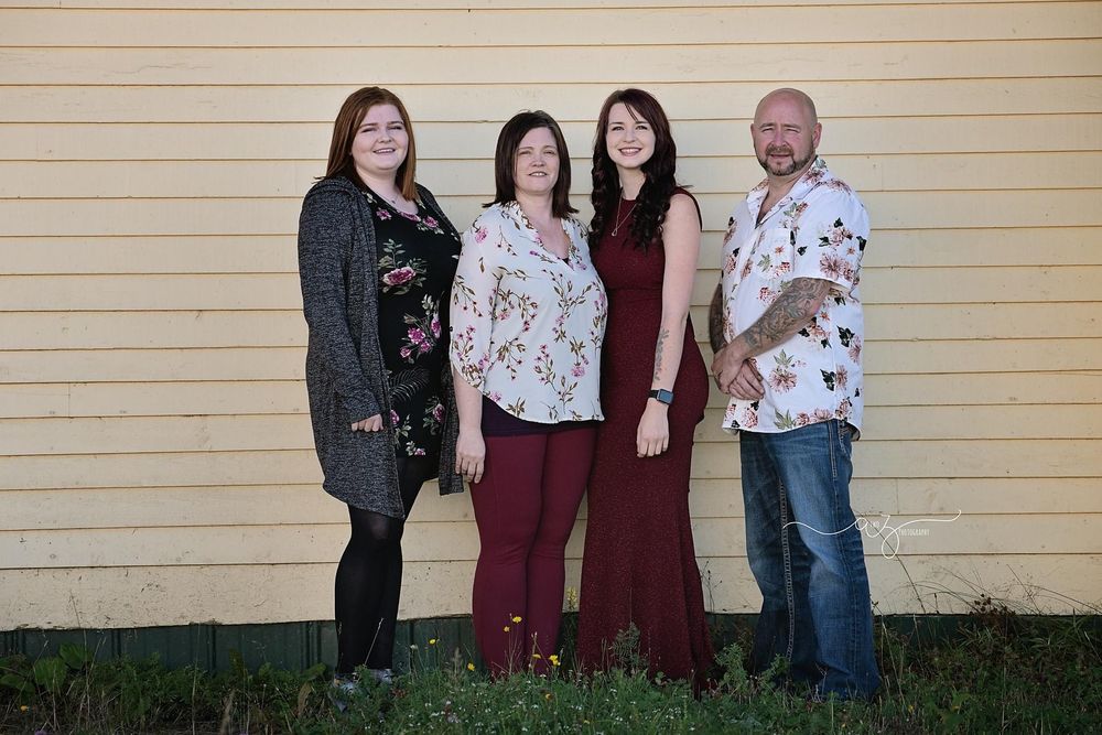 A group portrait of four people standing against a yellow wall outdoors.