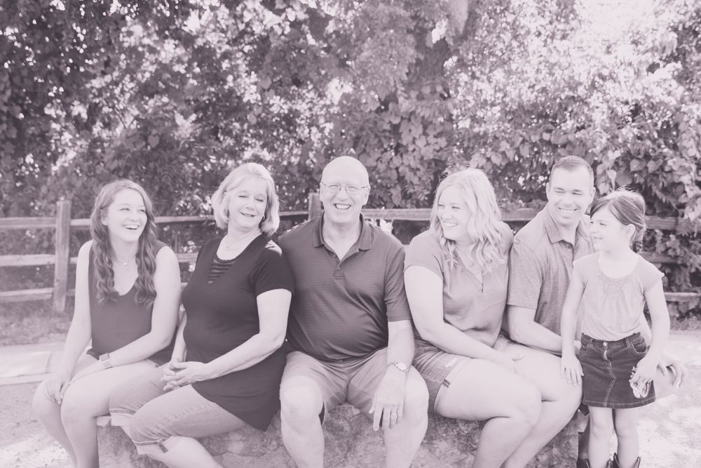 Black and white family portrait on wooden bench with natural background.