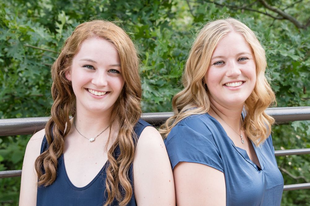 Two people with blonde and auburn hair sitting together outdoors in casual attire.