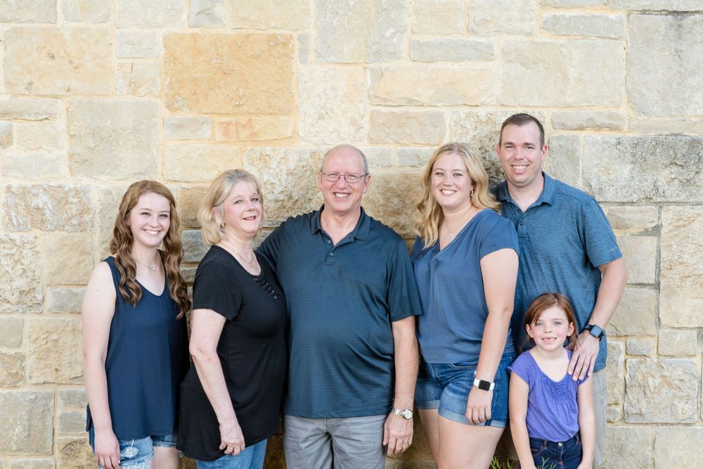 Family portrait against stone wall backdrop in casual summer clothing.