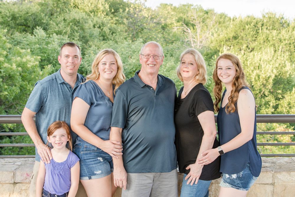 Family group poses together on outdoor deck with lush greenery in background.