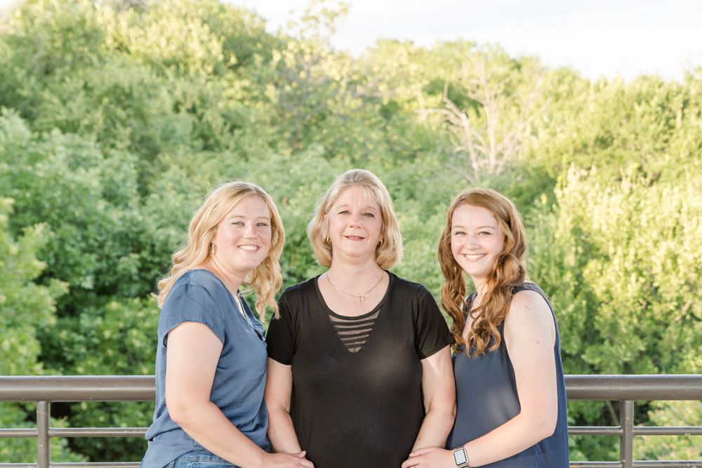 Three people in coordinated navy and black outfits pose together outdoors.