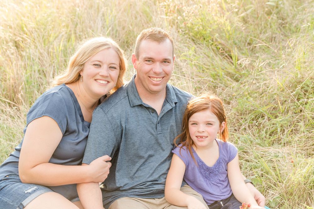 Three people pose together in sunlit field with natural golden background.