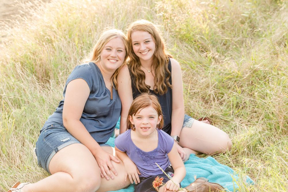 Three people sitting together on grassy hill in golden sunlight.