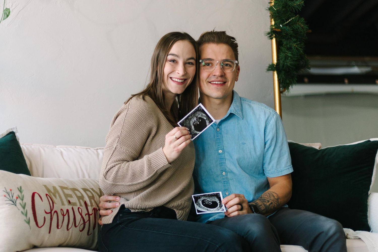 A couple sits on a couch holding ultrasound photos while sharing a joyful moment together.