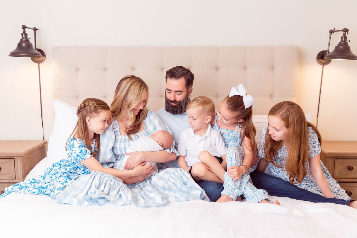 Family in coordinating blue and white outfits gather together on bed for intimate portrait.