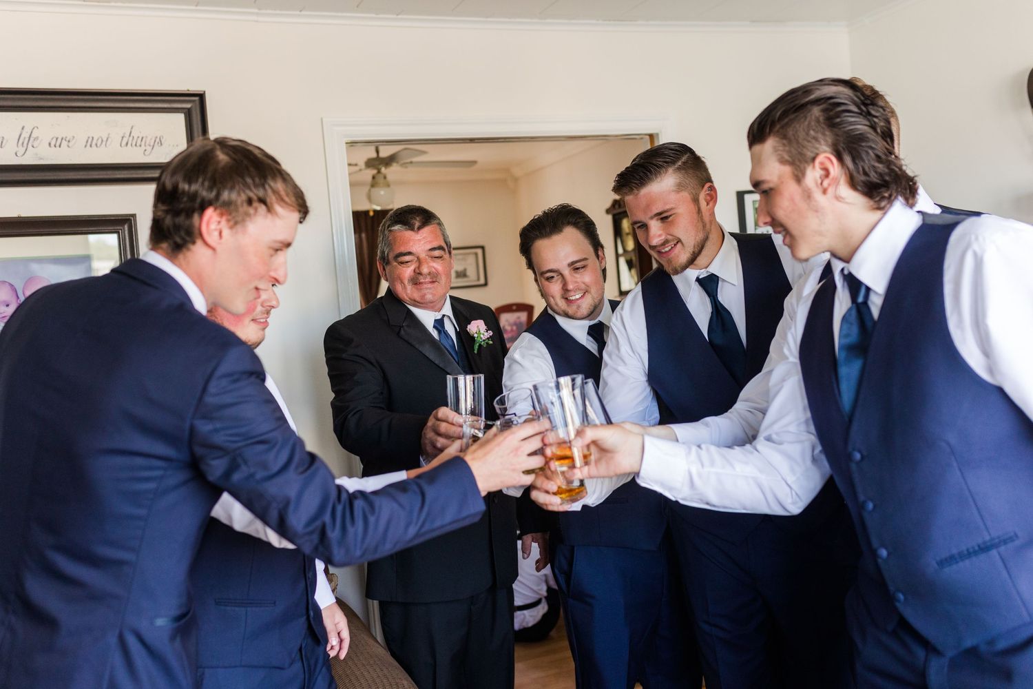 Groomsmen sharing drinks and laughs indoors while getting ready for a wedding.