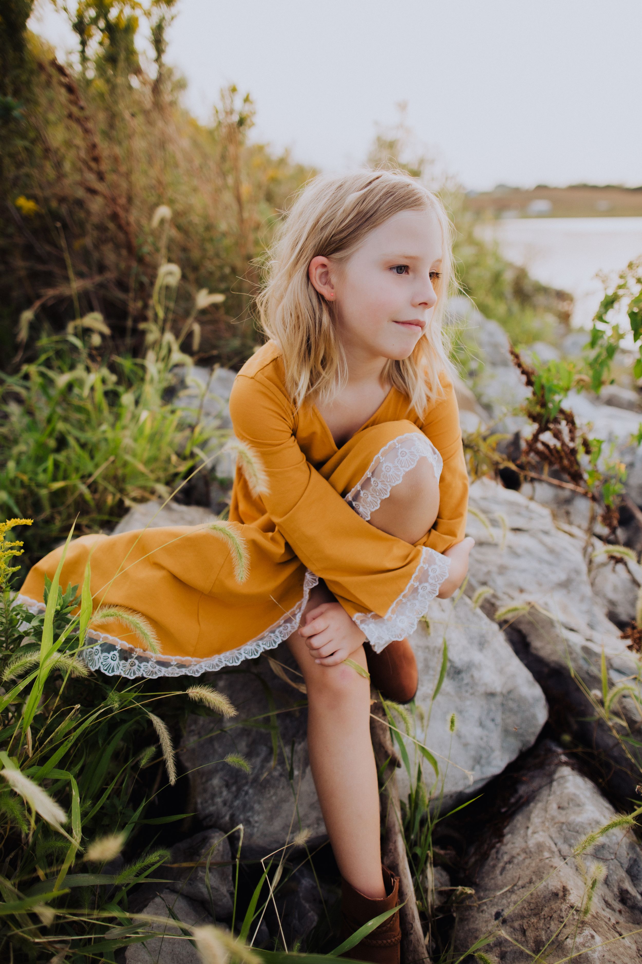 A mustard yellow dress contrasts with gray rocks and green foliage in an outdoor setting.