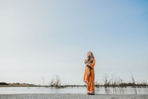 A figure in orange stands silhouetted against a serene lake landscape.