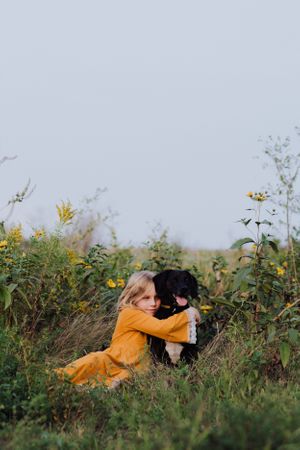 A black dog and someone in a yellow dress relax among wildflowers in a meadow.