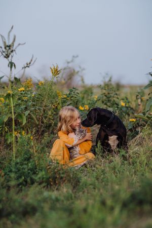 A serene outdoor portrait featuring a black dog and yellow dress among summer flowers.