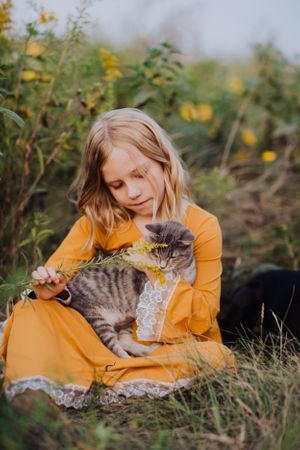 A tabby cat receives gentle pets while lounging in grass and yellow flowers.