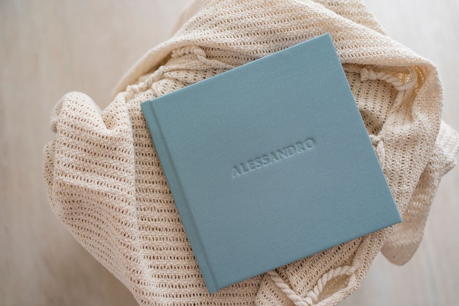 Personalized blue linen baby photo album embossed with name Alessandro wrapped in cream knit blanket.