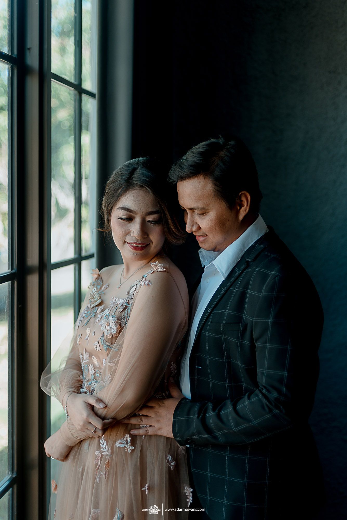 Romantic portrait of a couple by a window in formal attire.