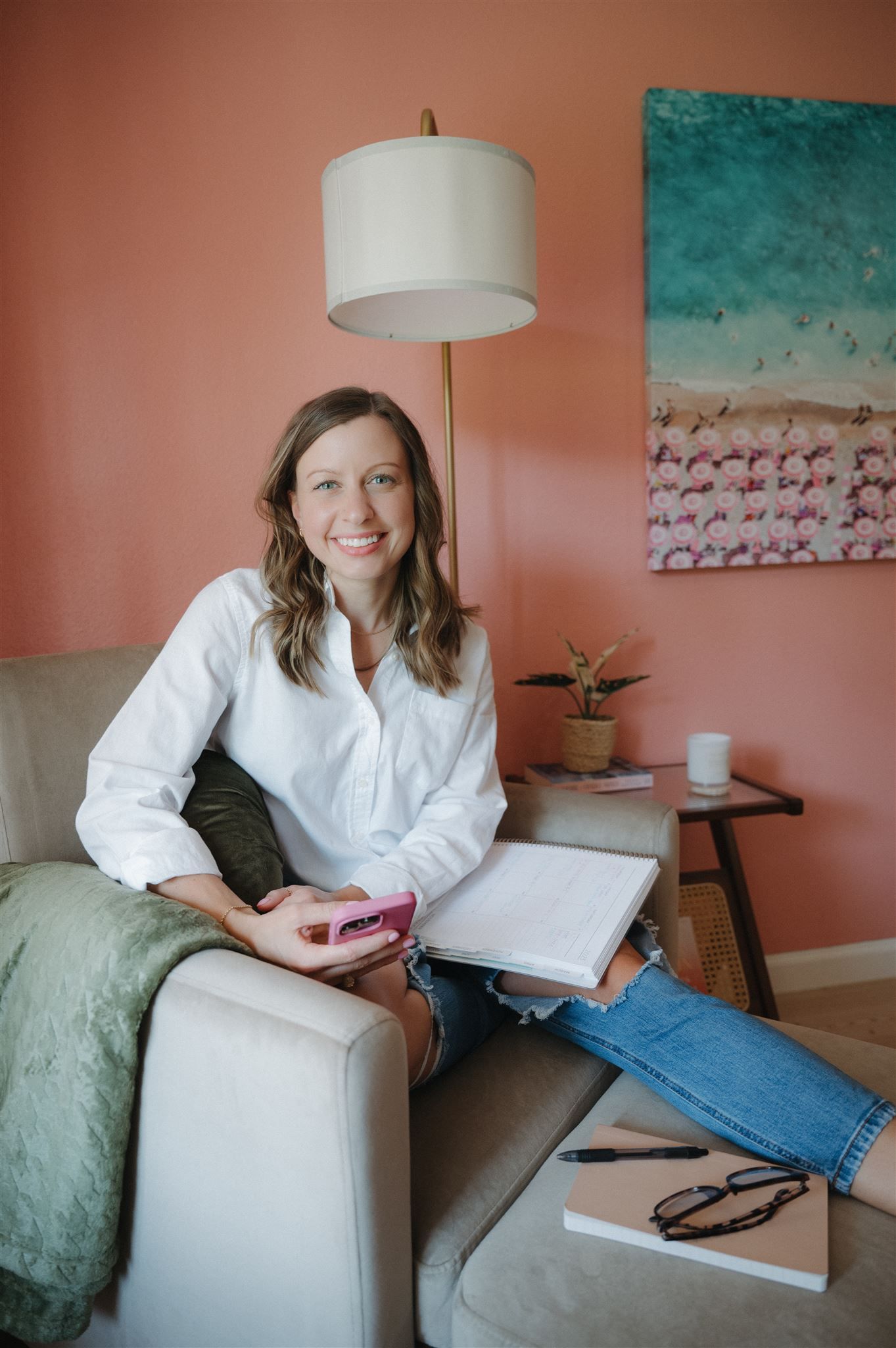 Person sitting on beige couch with laptop and green throw blanket by pink wall.