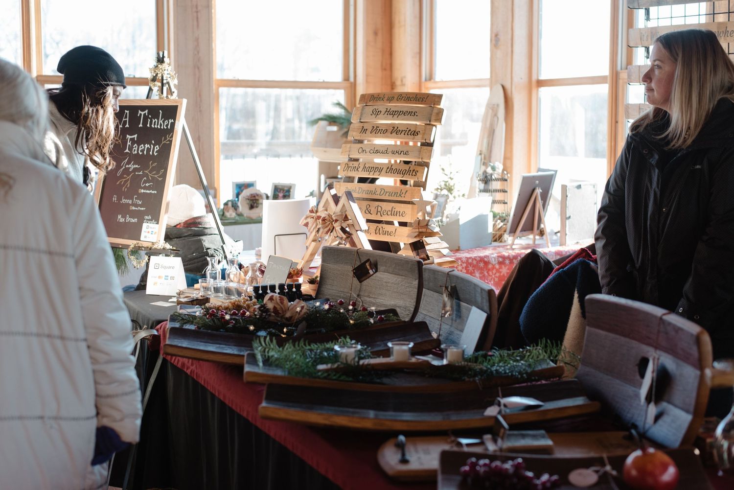 Holiday craft market display with wooden decor and festive items on a black tablecloth near sunny windows.
