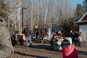 A crowd enjoys an outdoor winter event with smoke rising from cooking stations.