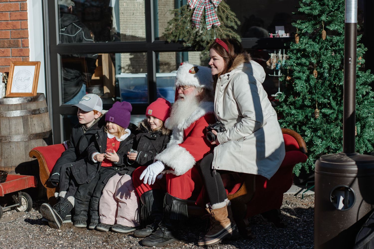 A group in winter coats gather on a bench outside a brick building during winter.