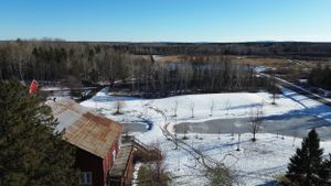 Aerial view of a snowy outdoor ice rink with red buildings and forest surroundings.