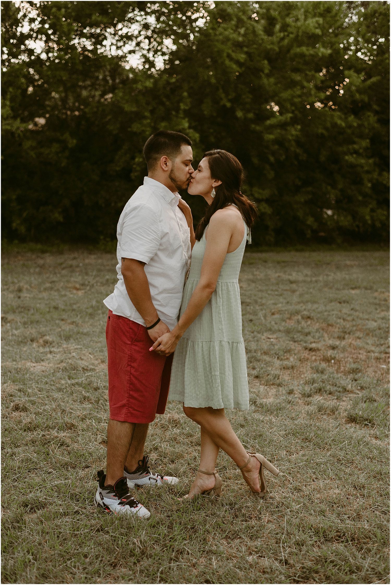 A couple in casual summer attire embracing in a grassy field at dusk.
