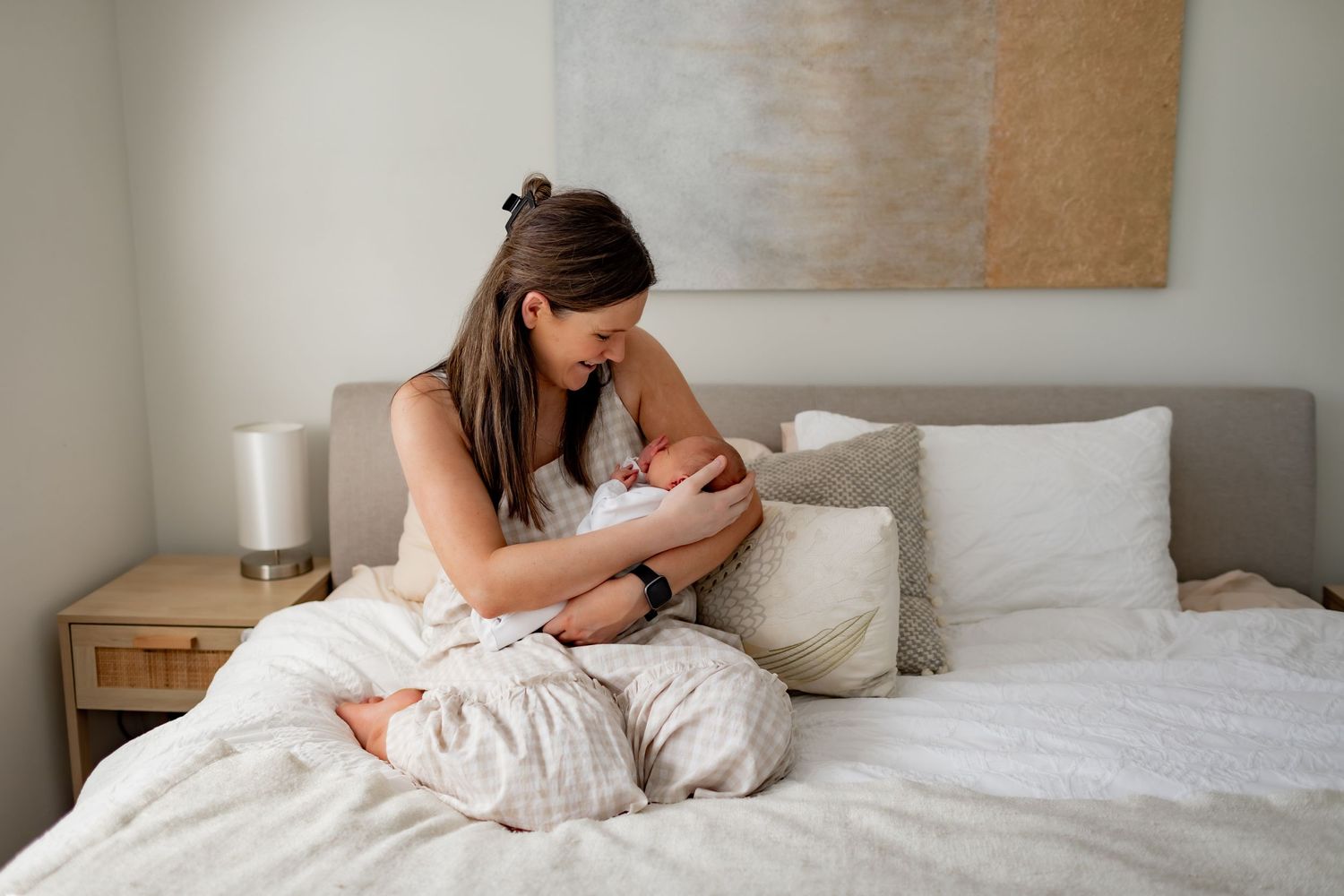 Intimate nurturing moment on a white bed with neutral decor and natural lighting.