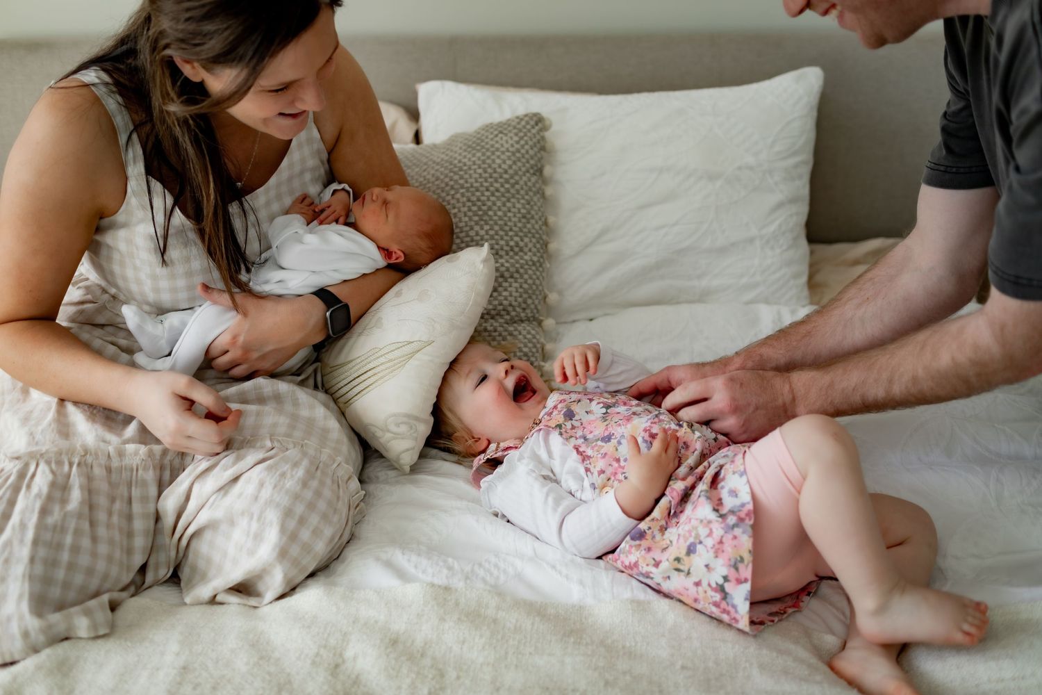 Parents tend to their baby while relaxing together on a white bed with soft linens.