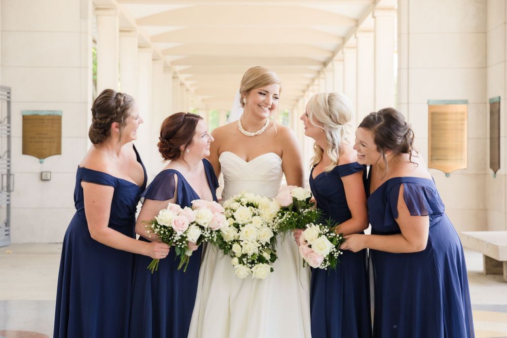 Wedding party gathers around bouquets in an elegant colonnade.