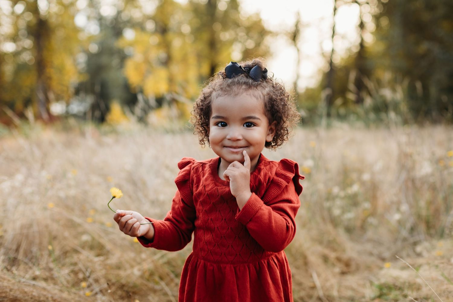 Cheerful child in red dress playing outdoors in tall autumn grass.