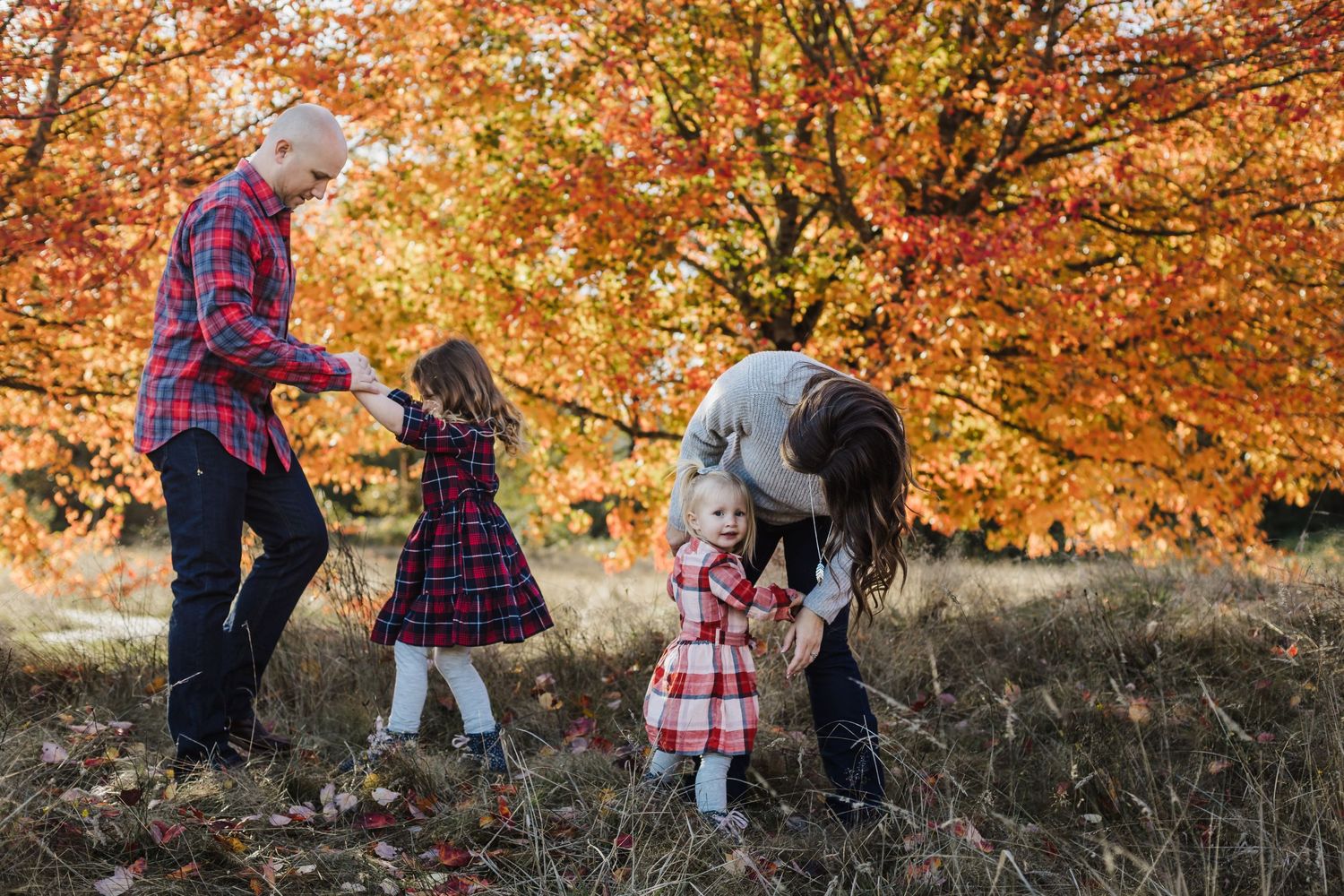 Family enjoying an autumn day together dancing in a field with orange fall foliage.