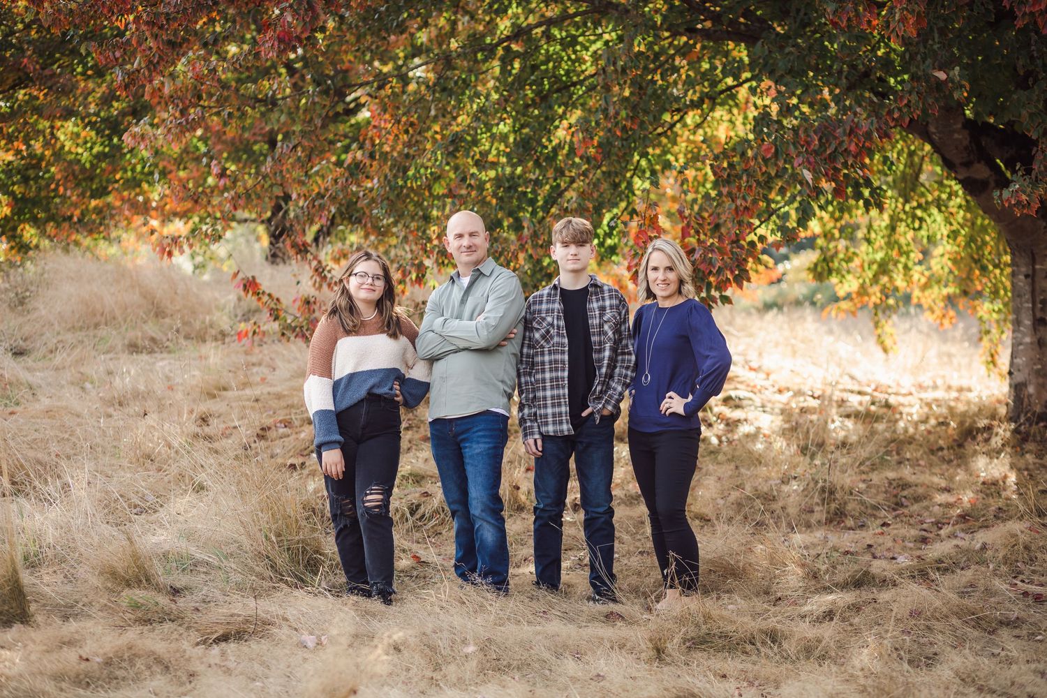 Family of four poses together under autumn tree in outdoor setting.