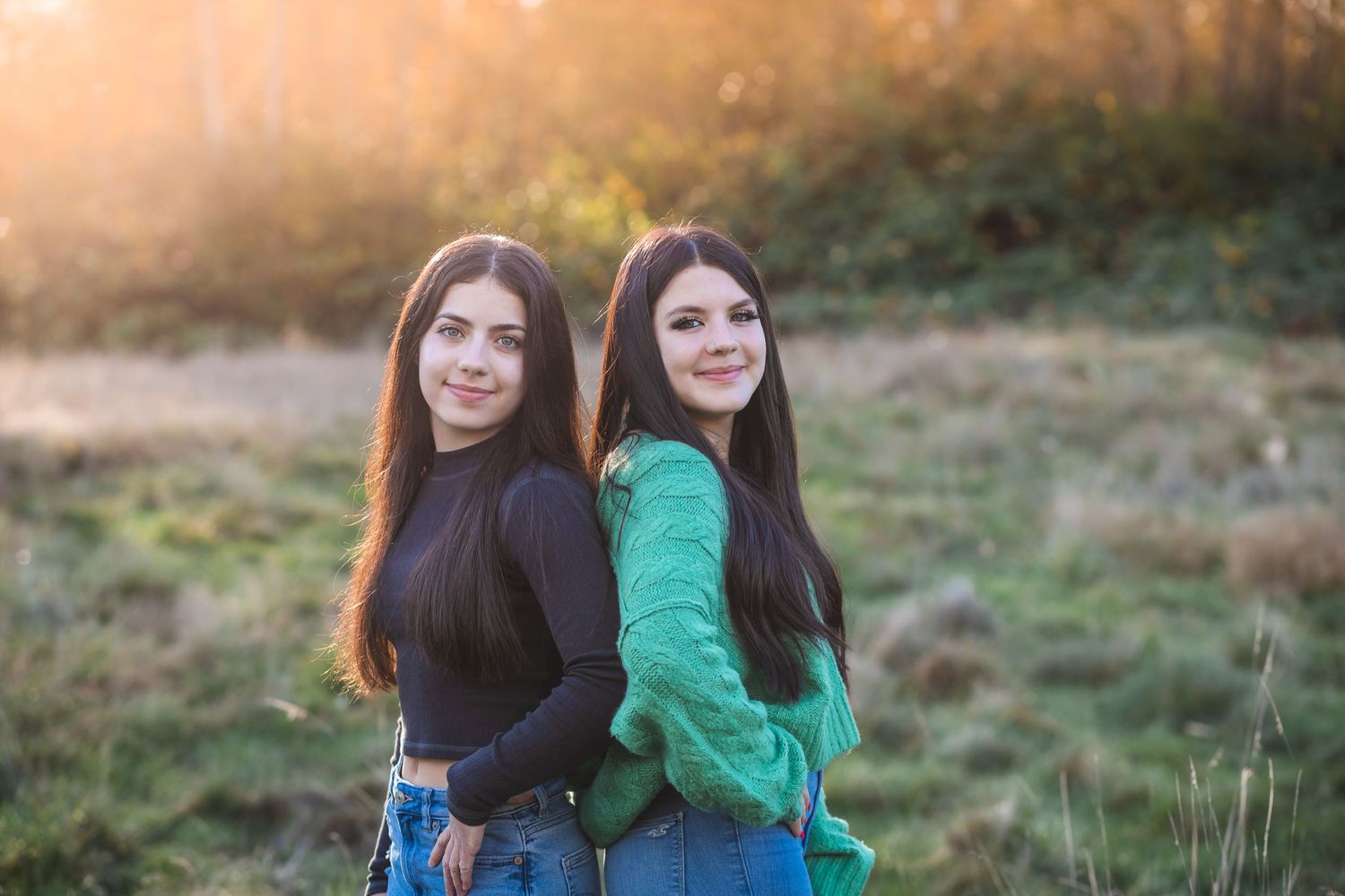 Two young women in casual attire pose together during golden hour.