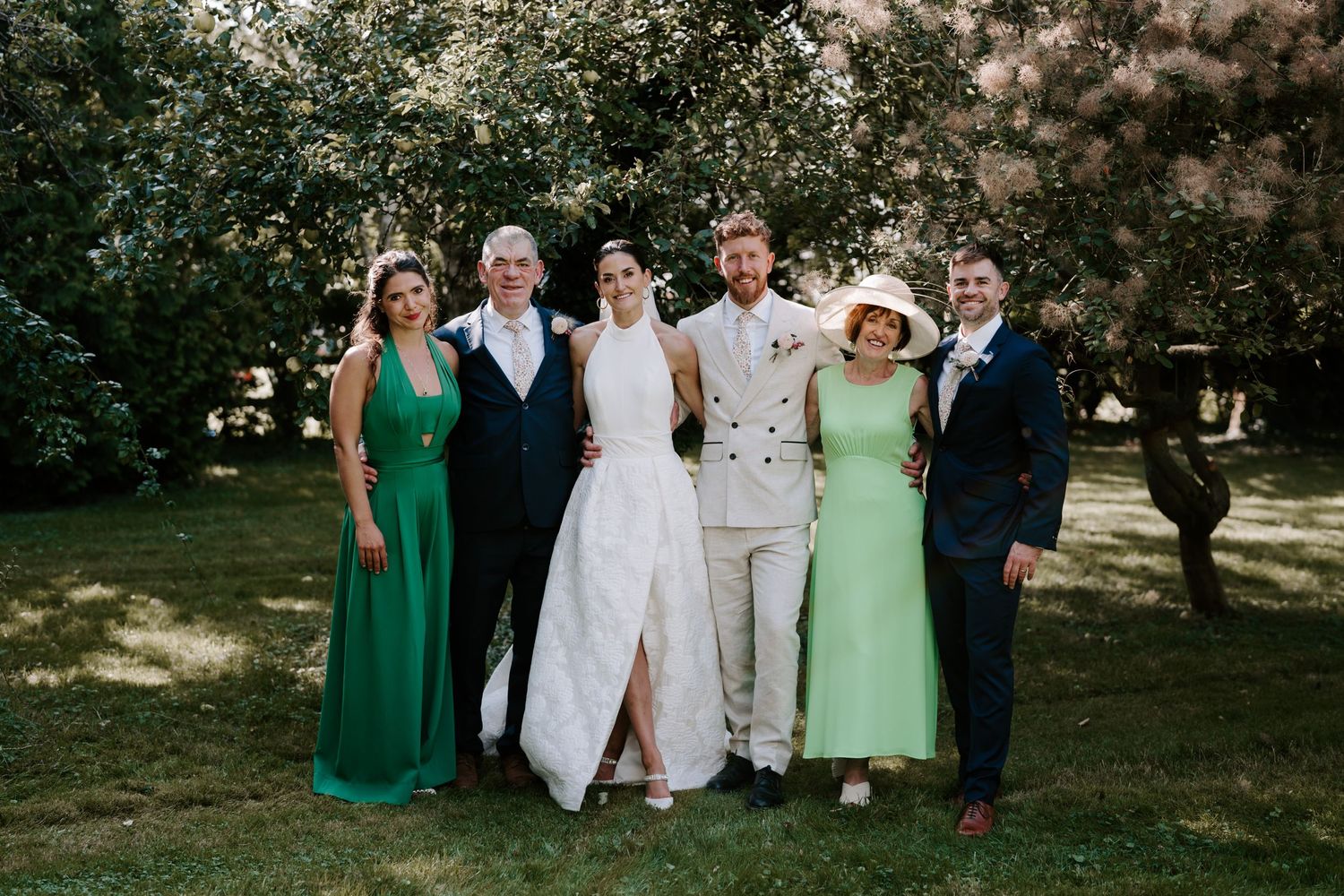 bride and groom with family smiling for a portrait in orchard in islip, oxfordshire