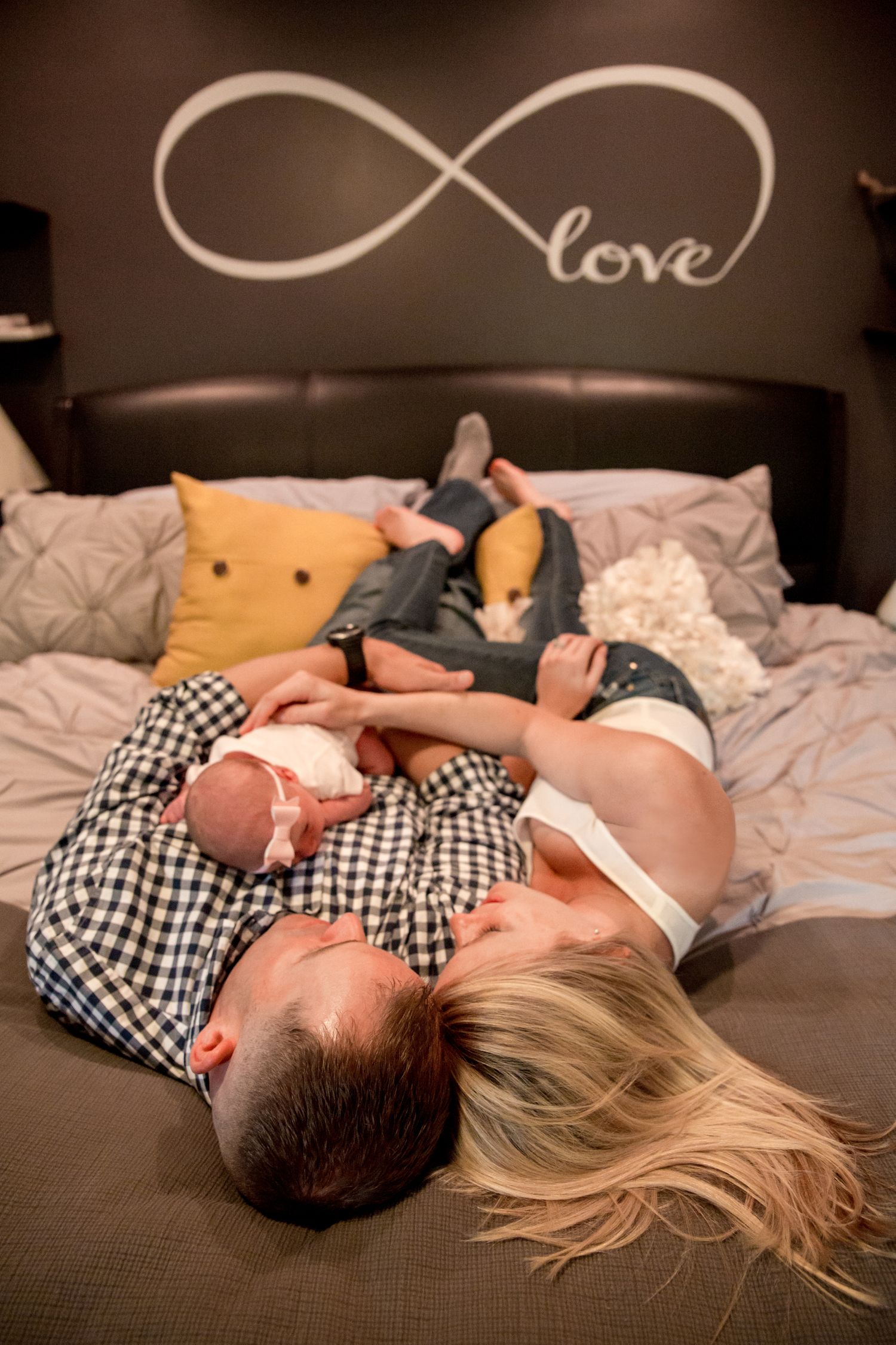New mom and Dad lay on bed with newborn baby on Daddys chest for Newborn Lifestyle photo session by DANIE Photography