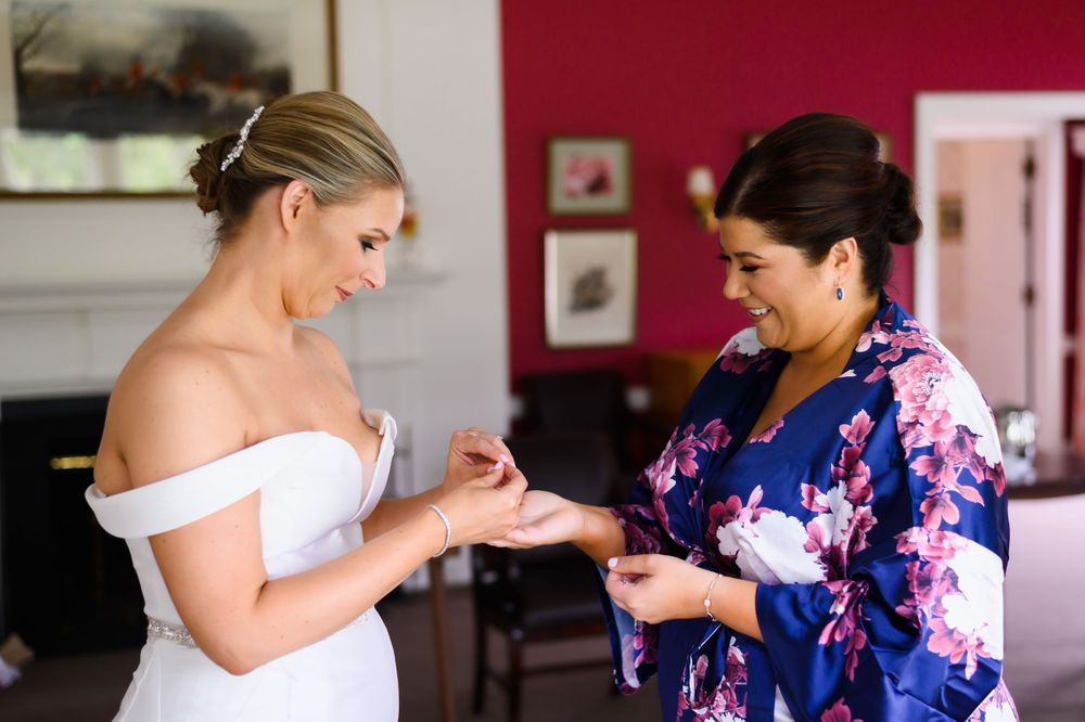 Bridesmaid helping bride with jewelry before wedding at Chagrin Valley Hunt Club in Ohio.