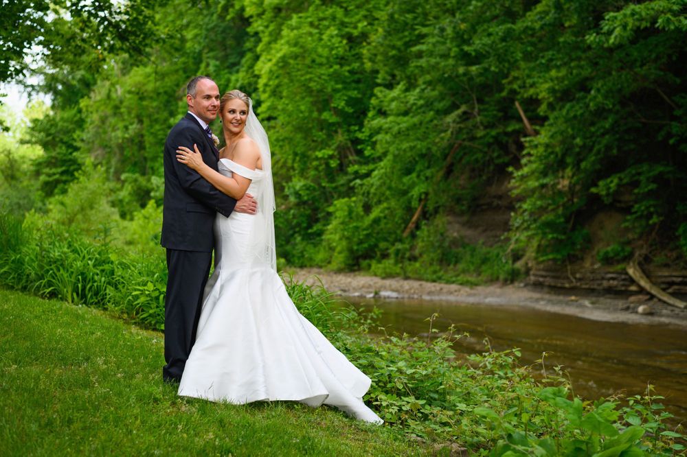 Bride and groom embrace by river during wedding day in Kirtland, Ohio.