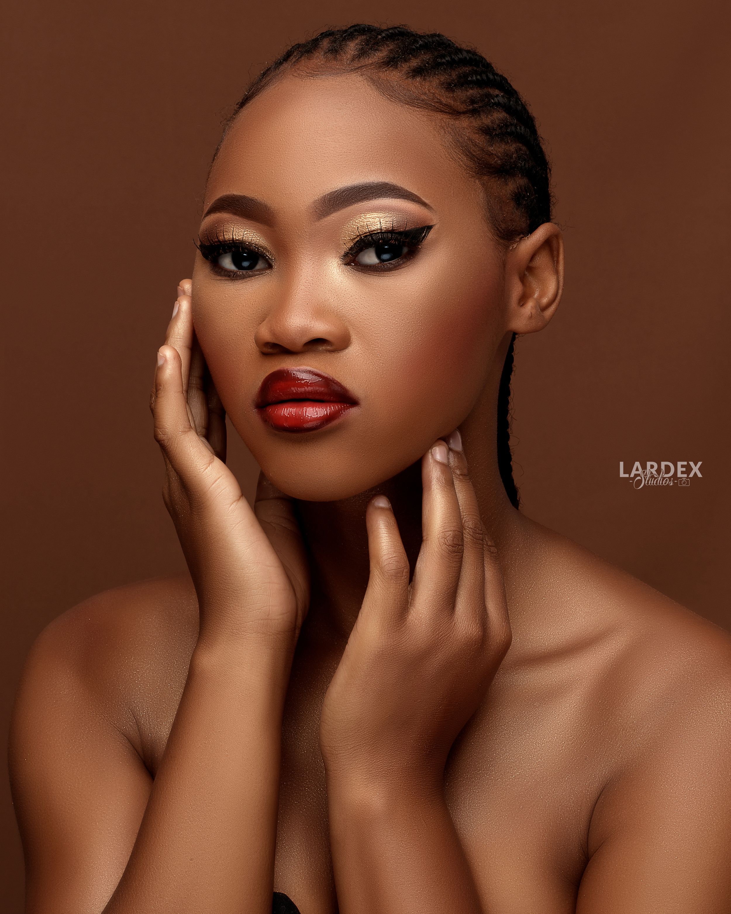 Dramatic beauty portrait highlighting bold red lipstick and intricate braided hairstyle against brown backdrop.