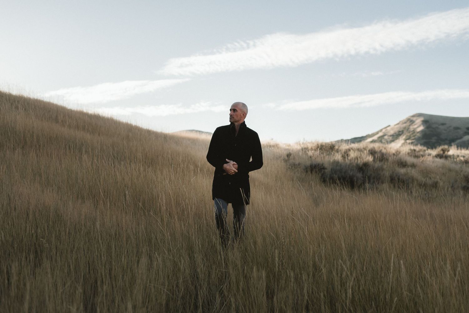 Figure walking through tall golden grass on a hillside at sunset.
