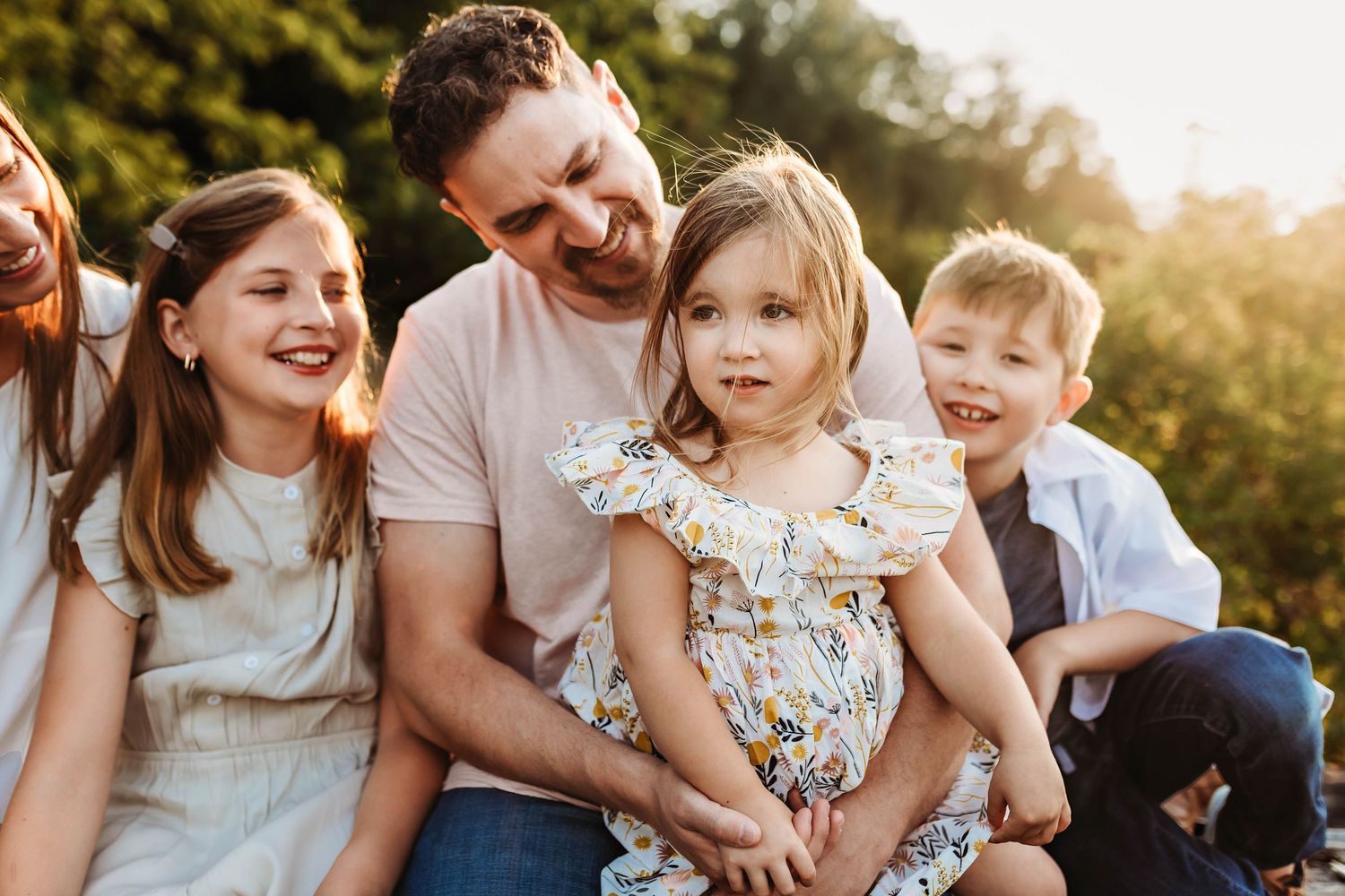 Family sitting together outdoors sharing joyful moments in warm sunset lighting.