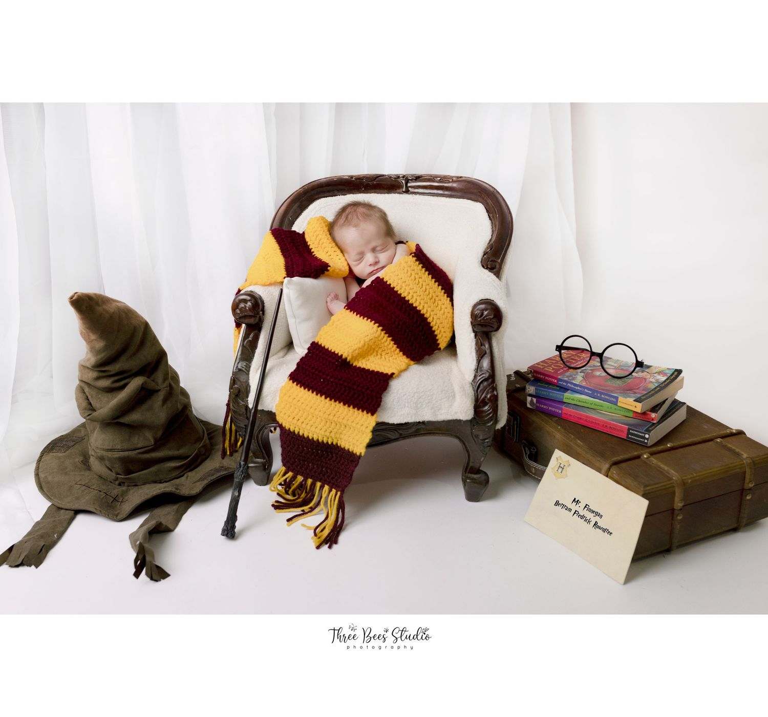 Harry Potter themed newborn photo setup with striped scarf, sorting hat, and magical books on antique chair.